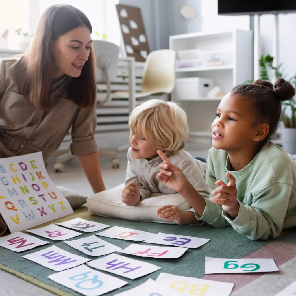 A group of preschool-aged children are engaged in an educational activity with a teacher on the floor, learning the alphabet.