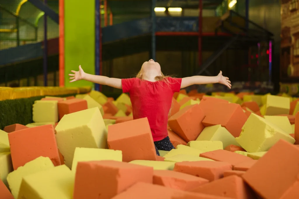 Kids and adults jumping at an indoor trampoline park with foam pits and basketball hoops.